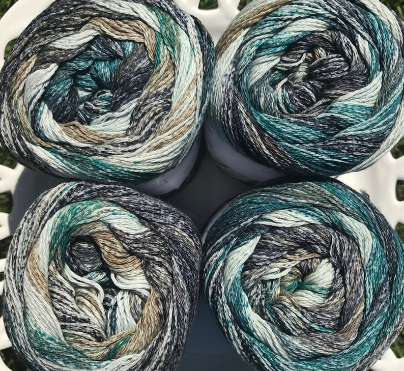May include: Four balls of yarn in a green, blue, brown, and white color pattern. The yarn is wound into balls and ready for knitting or crocheting.