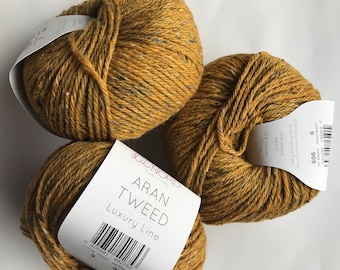 Könnte beinhalten: Drei Knäuel Aran Tweed Luxury Line Garn in Senfgelb mit blauen und grünen Sprenkeln. Das Garn wird in Italien hergestellt und besteht aus 50% Wolle, 30% Alpaka und 20% Viskose.