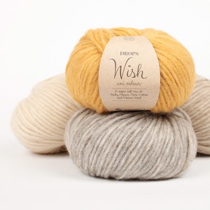 May include: Three balls of yarn in different colours: mustard yellow, light beige, and grey. The label on the top ball reads "DROPS Wish uni colour A super soft mix of Baby Alpaca, Pima Cotton and Merino Wool."