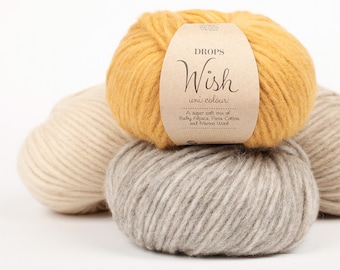 May include: Three balls of yarn stacked together. The top ball is mustard yellow with a paper label reading DROPS Wish uni colour, A super soft mix of Baby Alpaca, Pima Cotton and Merino Wool. The other two balls are beige and light gray.