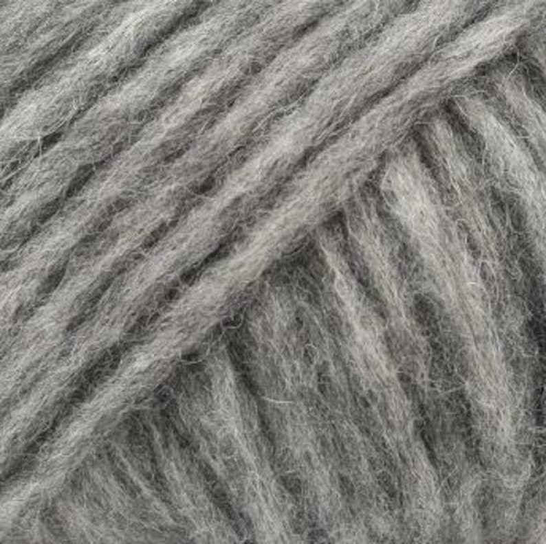 May include: A close-up view of light gray yarn featuring a multi-ply twisted construction. The fibers appear soft and slightly fuzzy with a consistent matte texture throughout the strands, showing the diagonal orientation of the spun wool yarn.