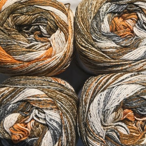 May include: Four balls of yarn in a brown, orange, white, and gray color pattern. The yarn is arranged in a square shape.