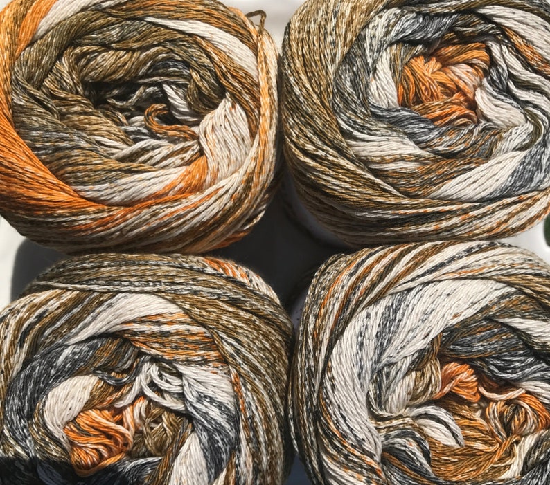May include: Four balls of yarn in a brown, orange, white, and gray color pattern. The yarn is arranged in a square shape.