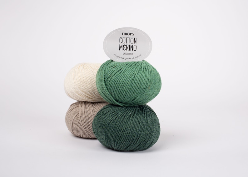 May include: Three balls of yarn stacked on top of each other. The bottom ball is beige, the middle ball is light brown, and the top ball is green. A white label with black text reads "DROPS COTTON MERINO UNI COLOUR A superwash yarn for all seasons."