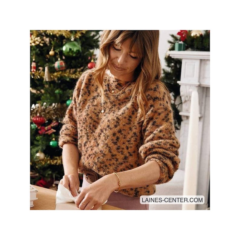 May include: A woman wearing a brown and black fuzzy sweater with a small gold pendant necklace and a gold bracelet. She is wrapping a gift with white paper.