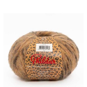 以下が含まれることがあります： ヒョウ柄のラベルが付いた茶色、黒、オレンジの糸のボール。ラベルには「Phil Leo Concept」と「Effet Imprime Leopardo」と書かれています。