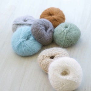 May include: Seven balls of yarn in various colors, including light blue, gray, beige, and green. The yarn is soft and fluffy, perfect for knitting or crocheting.