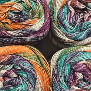 May include: Four skeins of yarn in a multi-colored pattern of orange, teal, purple, and white. The yarn is wound into balls.