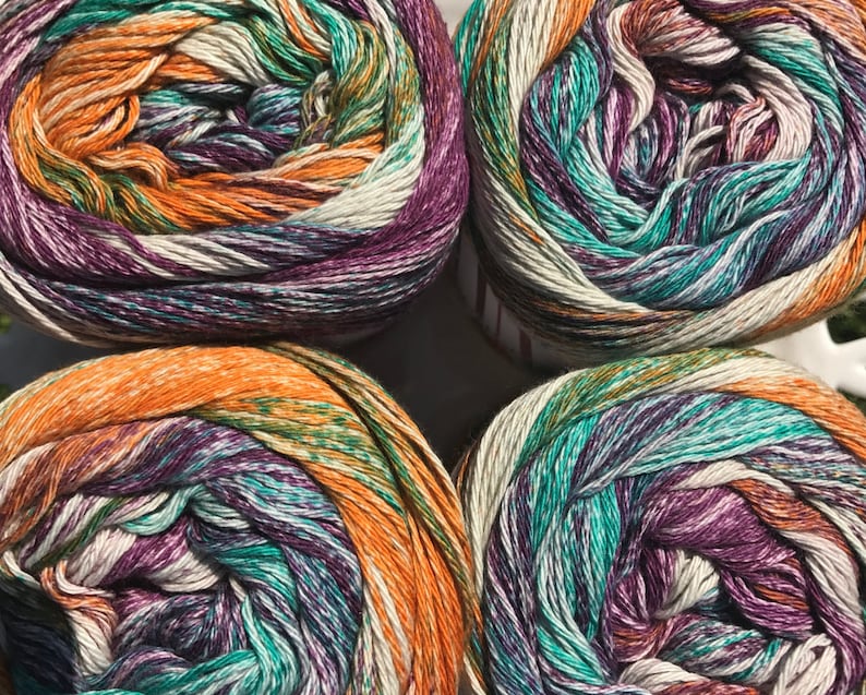 May include: Four skeins of yarn in a multi-colored pattern of orange, teal, purple, and white. The yarn is wound into balls.