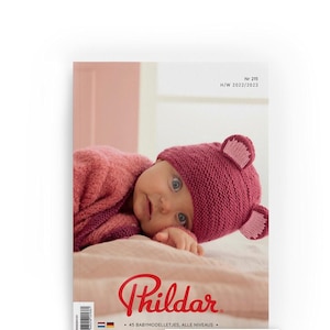 Può includere: Un bambino con un cappello rosa lavorato a maglia con orecchie da orso e un maglione abbinato è raffigurato sulla copertina di una rivista. La copertina della rivista riporta il testo "Nr 215 H/W 2022/2023" e il marchio "Phildar".