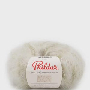 May include: A ball of fluffy, off-white yarn with a paper label featuring the red text Phildar, the product name PHIL LEO, and the phrase EFFET IMPRIME LEOPARD. The label includes a small swatch showing a light-colored leopard print pattern.