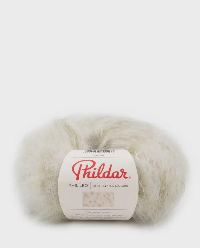May include: A ball of fluffy, off-white yarn with a paper label featuring the red text Phildar, the product name PHIL LEO, and the phrase EFFET IMPRIME LEOPARD. The label includes a small swatch showing a light-colored leopard print pattern.