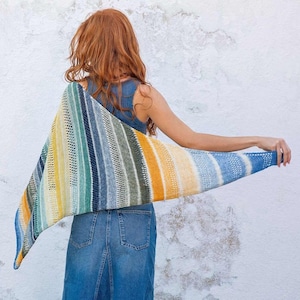 Puede incluir: Un chal triangular con un patrón de rayas en tonos de azul, verde, amarillo y blanco. El chal está hecho de un hilo suave y ligero y tiene un diseño delicado y calado.