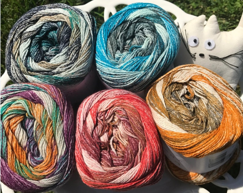 May include: Four skeins of yarn in different color combinations. The yarn is a mix of beige, orange, green, purple, blue, and gray. The yarn is wound into balls and is ready to be used for knitting or crocheting.