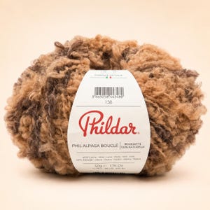 May include: A ball of Phildar Phil Alpaga Bouclé yarn in shades of brown and tan. The white paper label features the brand name, a barcode, and text stating 60% wool and 40% alpaca, with a weight of 50g or 1.76 oz, made in Italy.
