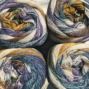 May include: Four balls of yarn in a white, purple, teal, and brown color scheme. The yarn is arranged in a circle on a white surface.