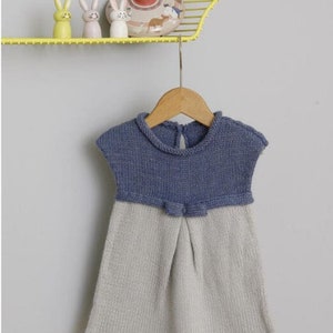 Peut inclure: Une robe en tricot bleu et gris pour b&eacute;b&eacute; avec un n&oelig;ud &agrave; la taille. La robe est suspendue &agrave; un cintre en bois.