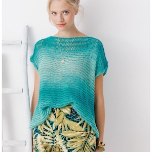 May include: A turquoise and light blue ombre knit top with short sleeves. The top is paired with shorts featuring a tropical leaf and leopard print. The model is wearing a gold necklace and bracelets.