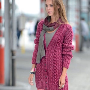 May include: A woman wearing a long, button-down, magenta cable-knit cardigan with a gray scarf. The cardigan has a textured pattern and long sleeves. She is also wearing a pink and red patterned skirt and a bracelet.