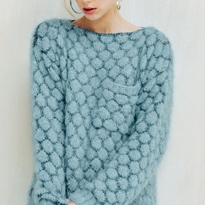 May include: A light blue sweater with a unique textured pattern. The sweater has a crew neck and long sleeves. The fabric appears soft and fuzzy. The sweater is a solid color and has a pocket on the front.