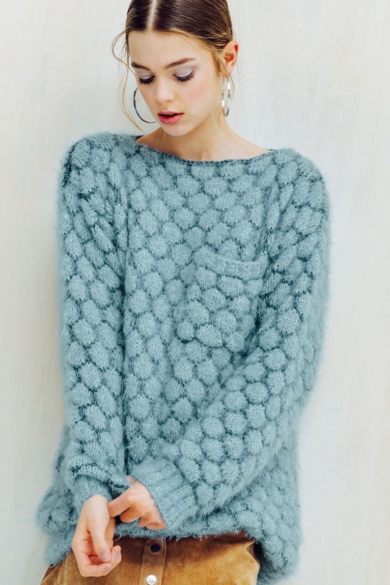 May include: A light blue sweater with a unique textured pattern. The sweater has a crew neck and long sleeves. The fabric appears soft and fuzzy. The sweater is a solid color and has a pocket on the front.