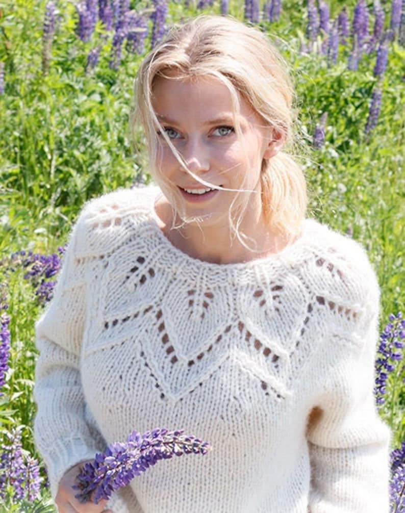 May include: A cream-colored, long-sleeved, hand-knitted sweater featuring a round neckline and a decorative, openwork leaf-patterned yoke. The garment is constructed with a chunky knit texture and ribbed cuffs, showcasing a detailed stitch design.