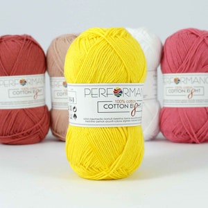 May include: A collection of colorful yarn skeins. The central skein is bright yellow, with a label reading "PERFORMANCE COTTON EIGHT 100% cotton." Other skeins are in shades of pink, white, and tan. The yarn is tightly wound and appears soft.