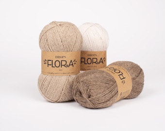 Pode incluir: Três novelos de lã em bege, castanho e branco. A lã está etiquetada com "DROPS *FLORA* MIX" e "DROPS *FLORA* UNICOLOUR".