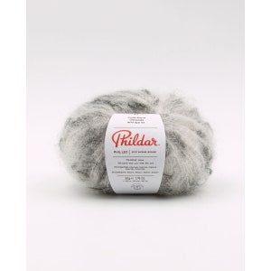 May include: A ball of fuzzy, variegated gray and white yarn with a white paper label featuring the red Phildar logo, the text PHIL LEO, and composition details including 71% mohair, 10% wool, 17% polyamide, and 2% elastane, weighing 1.76 ounces.