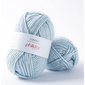 May include: Two light blue yarn skeins. The front skein has a white label with the text "FRIMAS 100% Motives naturelles phildar". The yarn is thick and appears soft, suitable for knitting or crochet projects.