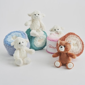 May include: Three plush cream-colored lamb toys and one brown bear toy arranged with four large, round skeins of soft, textured yarn in blue, teal, pink, and brown. One pink yarn skein features a white label with the brand name Phildar printed.