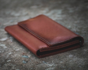 May include: A brown leather wallet folded closed. The wallet is lying on a rough, gray surface.