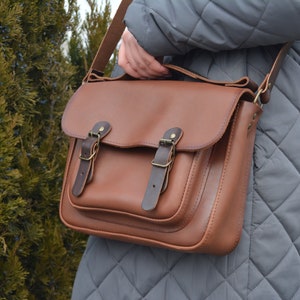 leather satchel, adjustable strap, one large pocket outside, one pocket inside, closed on flap and two fake magnet, top handle