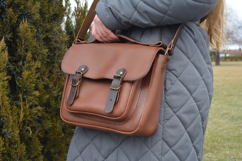 leather satchel, adjustable strap, one large pocket outside, one pocket inside, closed on flap and two fake magnet, top handle