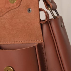 Pu&ograve; includere: Borsa a tracolla in pelle marrone con chiusura a patta e chiusura magnetica. La borsa ha un design strutturato con cuciture a vista e finiture metalliche. Il cinturino &egrave; fissato con anelli metallici.