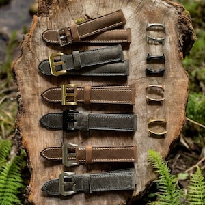 May include: Six leather watch straps in brown and grey colours, with different buckle styles. The straps are arranged vertically on a wooden surface.
