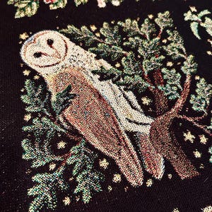 May include: A tapestry featuring a white barn owl perched on a branch with green leaves and gold stars on a black background.