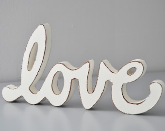 May include: White wooden sign with the word "love" in a cursive font.