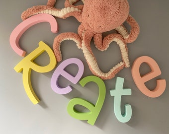 Könnte beinhalten: Ein rosa Plüsch-Oktopus mit weißen Verzierungen liegt auf einer grauen Oberfläche mit bunten Holzstempeln, die das Wort "create" buchstabieren.