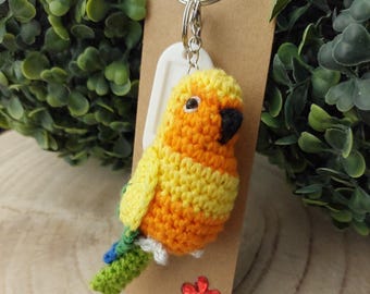 Könnte beinhalten: Ein gehäkelter gelber und orangefarbener Vogel-Schlüsselanhänger mit grünem Schwanz und einem weißen Etikett. Der Schlüsselanhänger ist an einem silbernen Schlüsselring befestigt.