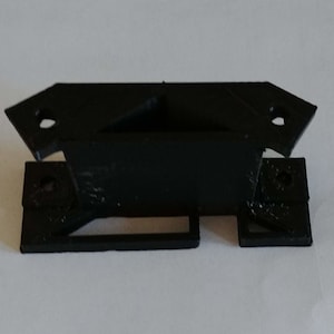 May include: A black plastic 3D printed part with a rectangular shape and two holes on each side. The part has a small rectangular opening in the center.