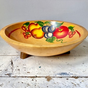 May include: A wooden bowl with three legs, painted with a fruit design. The bowl is painted with red, yellow, and green fruits, including apples, cherries, and grapes.