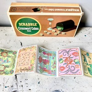 May include: A vintage Scrabble Crossword Cubes game box with a colorful illustration of the game board and dice. The box is beige with red and black lettering. The game is made by Selchow & Righter.