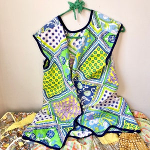 May include: A green, blue, and yellow patchwork fabric apron with a navy blue trim. The apron is hanging on a green wire hanger.