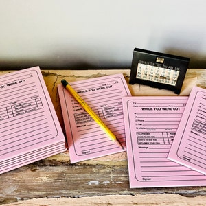 Peut inclure: Une pile de blocs-notes roses "While You Were Out" avec un crayon jaune sur l'un des blocs-notes. Les blocs-notes ont un design noir et blanc et comprennent des champs pour la date, l'heure, le numéro de téléphone, le message et la signature.