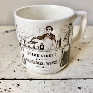 May include: White ceramic mug with a black and white illustration of a store front with the text "Solon Caddy's Fine Groceries, Wines, &c.&c."
