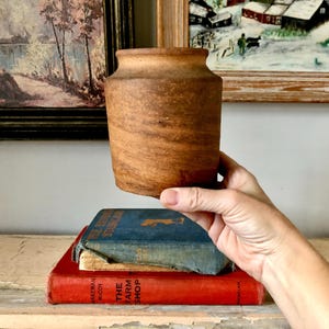 May include: A brown ceramic vase with a rounded shape and a slightly flared lip. The vase is sitting on top of two books.
