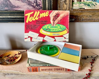 May include: Vintage "Tell Me" quiz game box with red, yellow, and green accents. The box reads "The Grand Quiz Game" and "Lots of fun for any number of players." The game includes a green and yellow spinner, cards, and a white box.