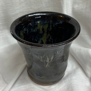 May include: A dark brown ceramic pot with a flared rim and a mottled glaze. The glaze has a dark blue and green color.