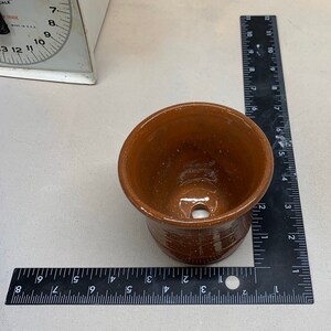 May include: A terracotta coloured ceramic pot with a drainage hole in the bottom. The pot is approximately 7.5 cm in diameter.